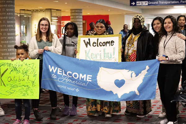 Larrge group of people holding welcome to America signs in an airport.