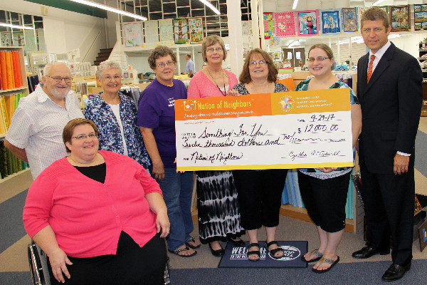 Photo of  Mary Neece, and standing Ed Smith, Alice Brown, Carol Amos, Jolene Smith, Cindy and Katie Koll, and Curt Zeck with big check