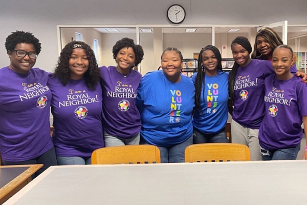 Group of eight smiling women inside a library, six wearing purple shirts and two in the middle right wearing blue shirts.