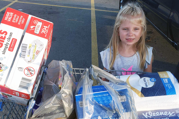 Photo of little blonde girl with grocery cart full of diapers and kleenex.