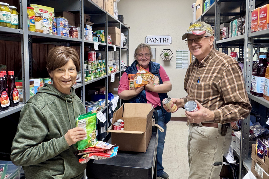 Three happy people in a food pantry holding various food items.