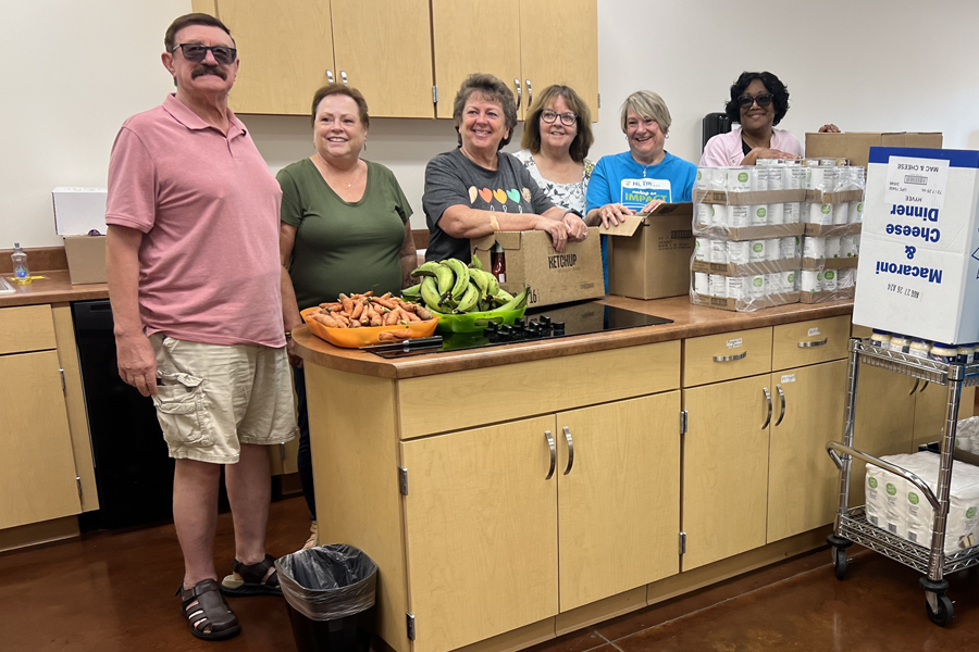A group of happy people in a kitchen with food, boxes, and canned goods.