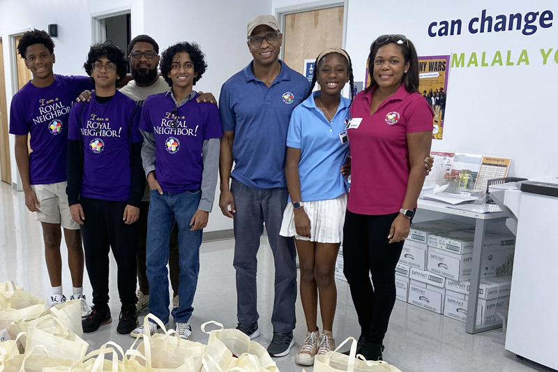 Group of smiling people behind severral tote bags of food.