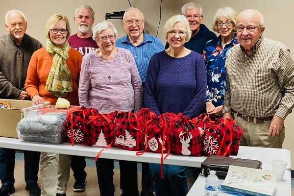 Group of happy people with festive bags and items on a table in front of them.