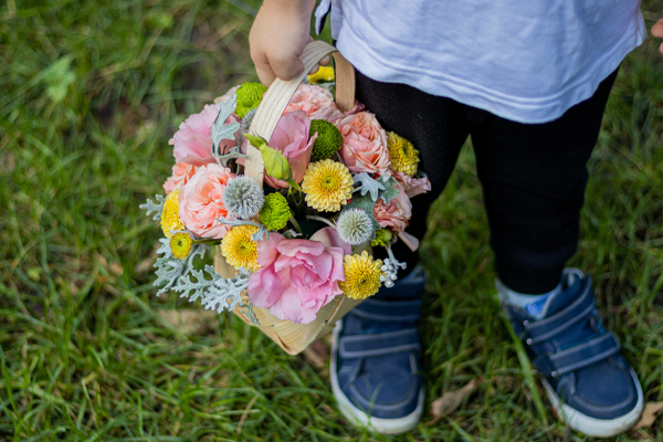 A child holding a colorful flower basket outside on grass.