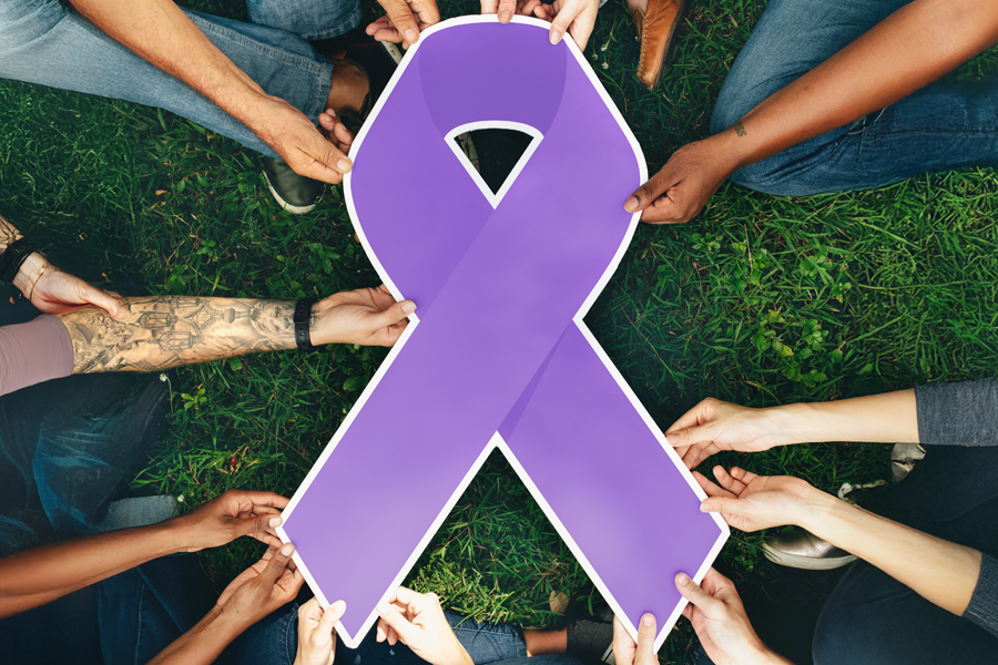 Group of diverse people on ground holding purple ribbon cut-out.