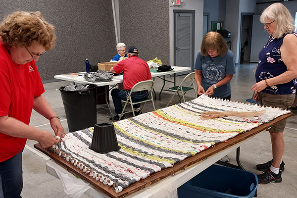 People weaving plastic bags into table-sized mats.