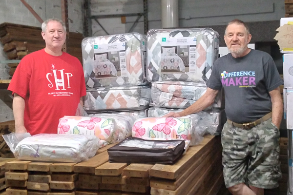 Two happy men in a warehouse wiith comforters.