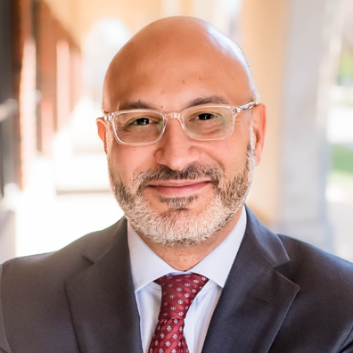 photo of Smiling man in a gray suite with red tie and glasses outside.
