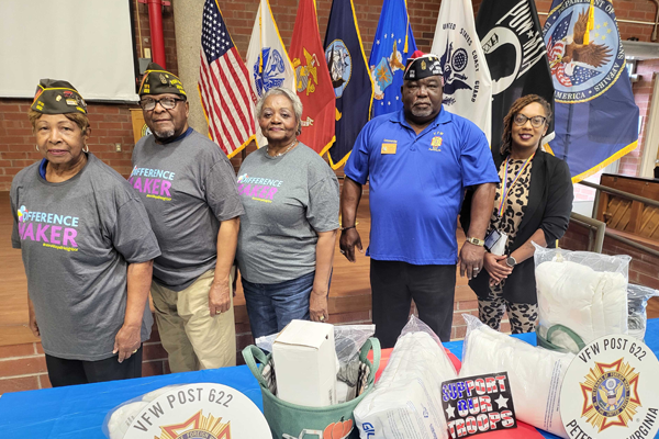 Five people standing in front of flags and begind a table in support of Veterans.