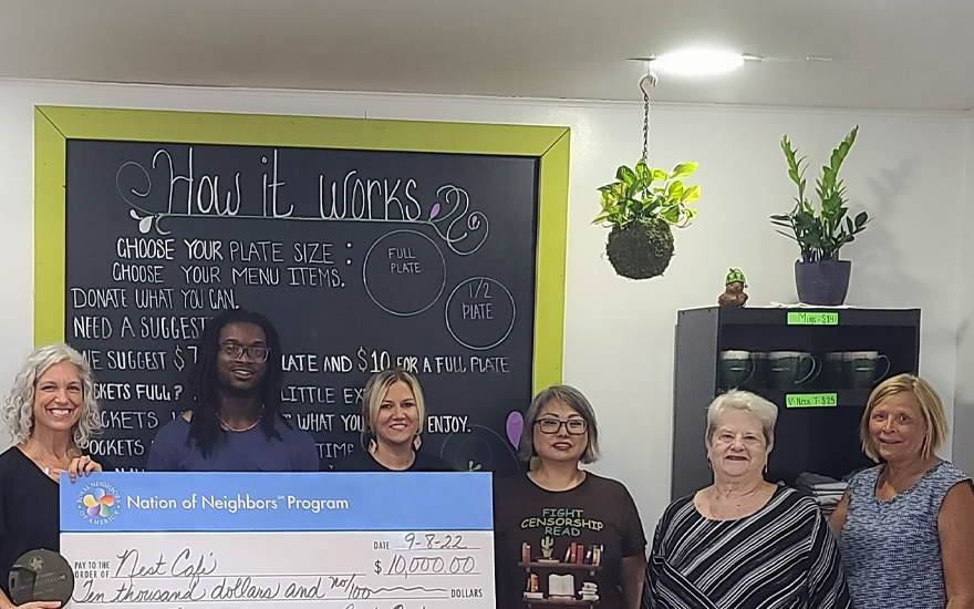 Group of happy people holding a giant $10,000 check inside a restaurant.
