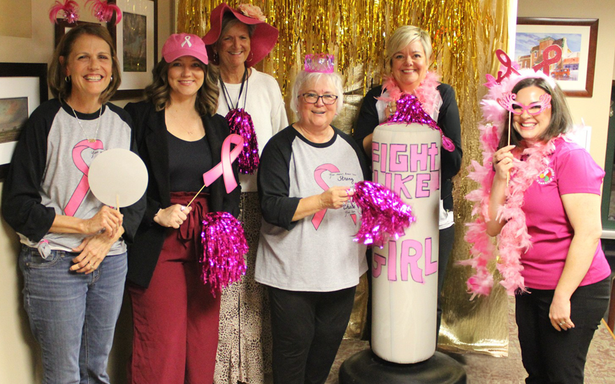 Group of happy women wearing pink and pink props in front of gold curtain.