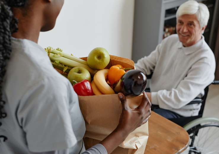 Woman carrying in groceries for a happy elderly man neighbor in a wheelchair.