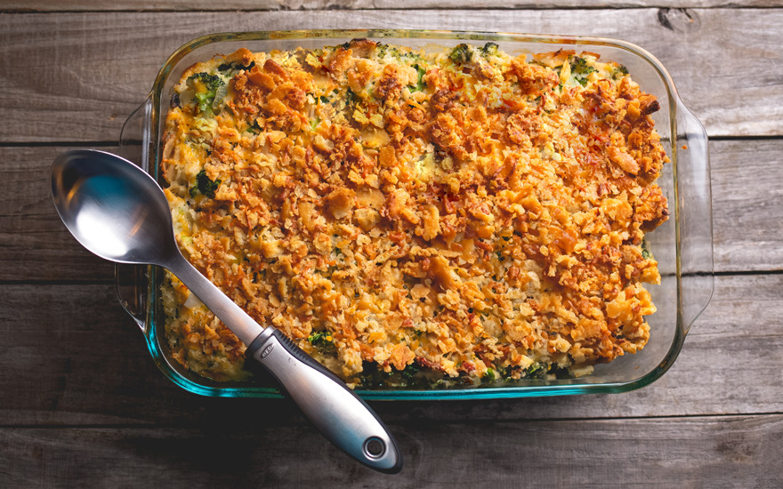 Broccoli-Corn Bake in a glass dish with a silver spoon on top, on a rustic, gray wooden table.