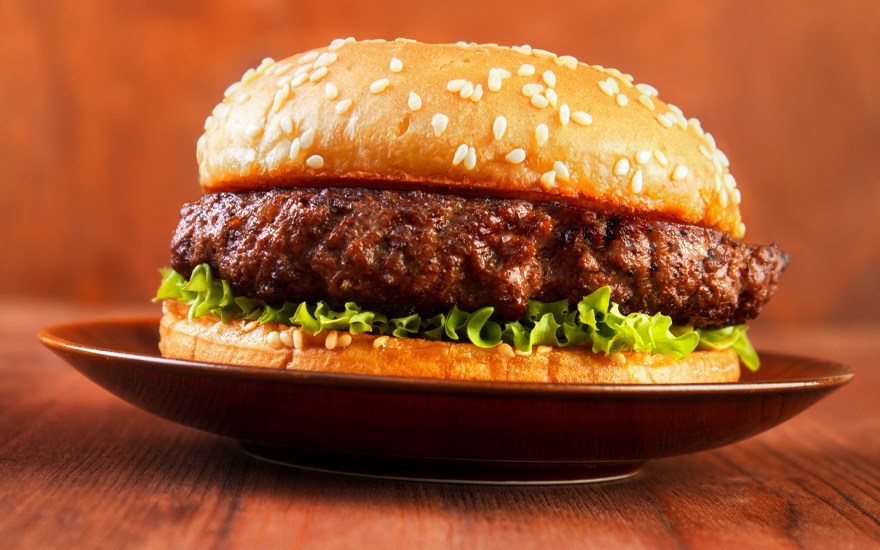 Onion Soup Hamburger on a sesame seed bun with lettuce on plate on wooden table.