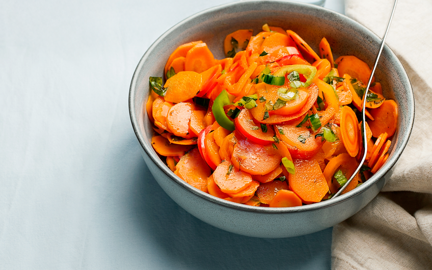 Close up of a light gray-blue bowl of sliced carrots with chopped up green peppers and chives.