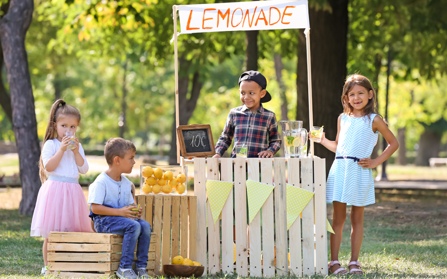 Diverse children at a lemonade stand in a park.