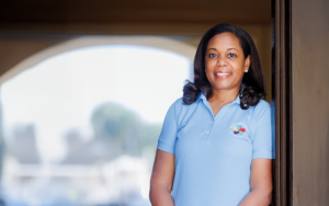 Smiling woman in a light blue Royal Neighbors polo leaning on a brown wall outside.