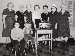 Black and with photo of a group of woman and children, one with headphones on.