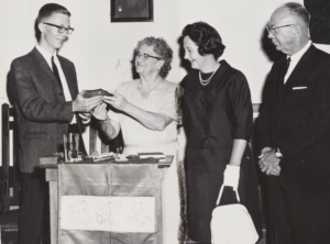 Black and white photo of a young man student accepting a scholarship with three adults.