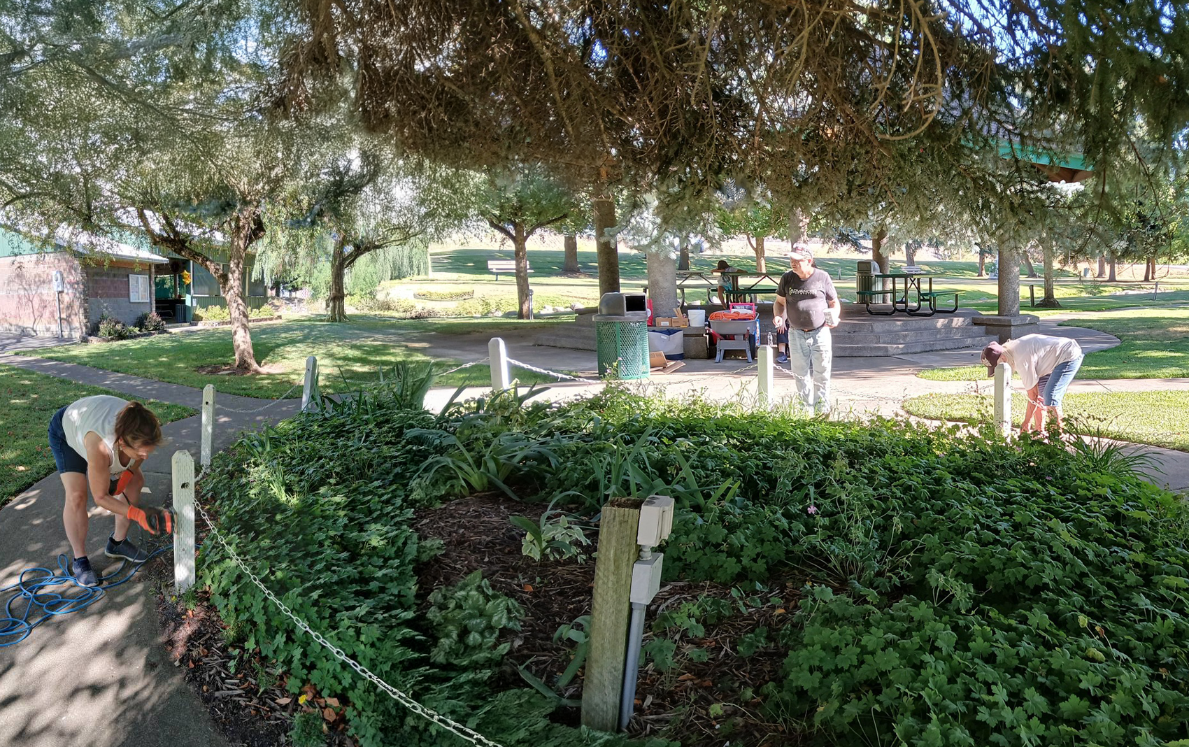 Three people working on sanding and painting flower bed posts at a park.