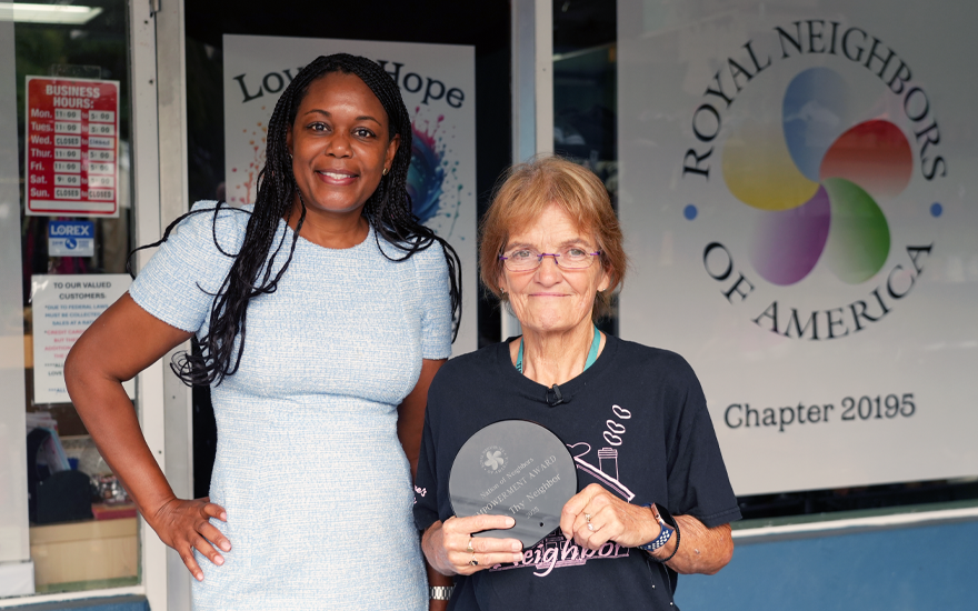 Two happy women outside of a thrift shop, one holding a Nation of Neighbors award.