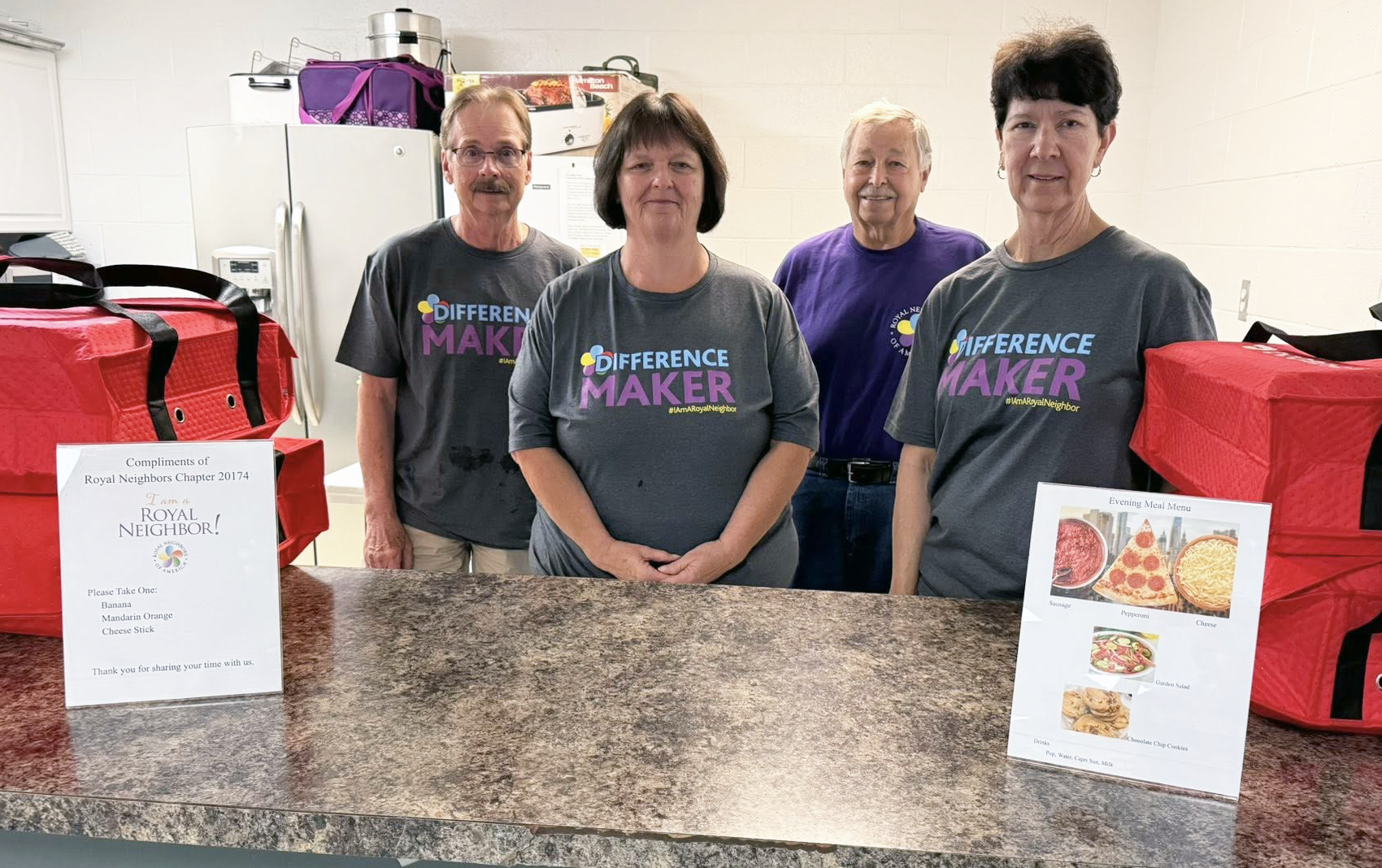 Four happy people behind a counter with pizzas in warmer bags.