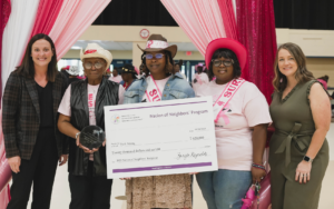Group of happy women with a large check and award in front of pink curtains.