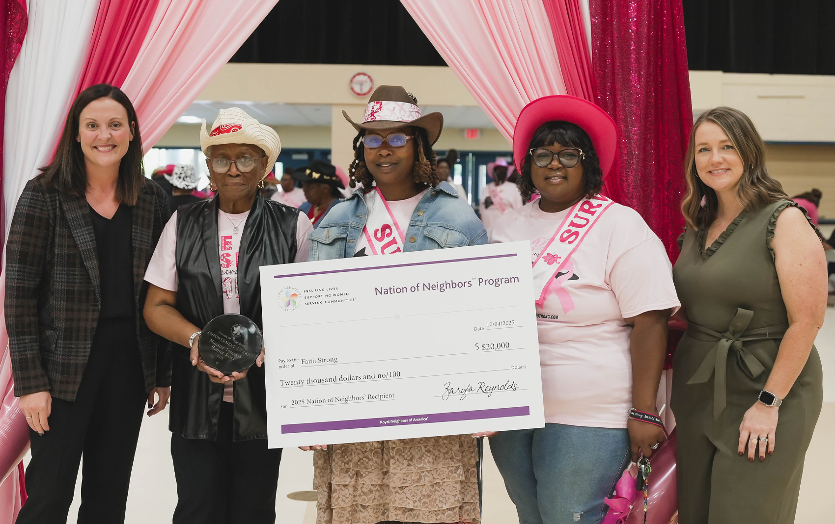 Group of happy women with a large check and award in front of pink curtains.