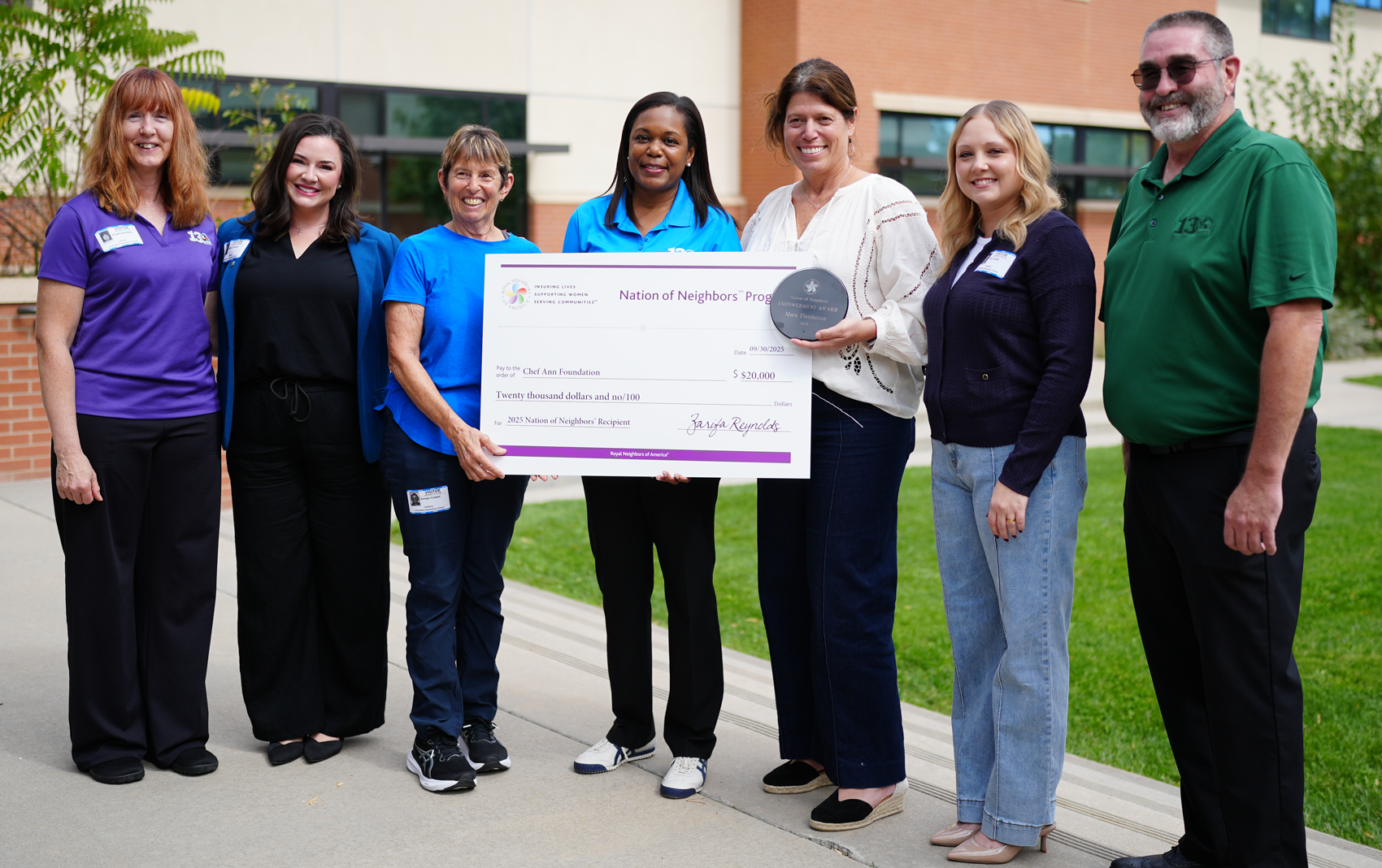 Group of happy people outside with a giant check and award.