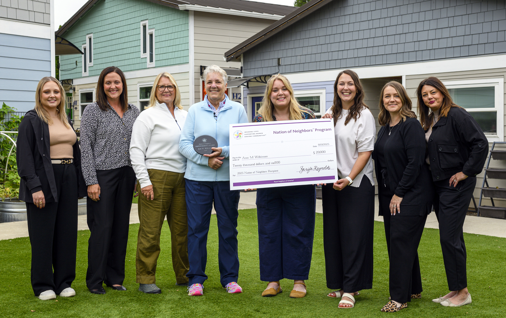 Several happy women outside with an award and giant check.