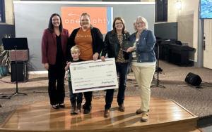 Four happy woman and male child holding a giant check on a stage.