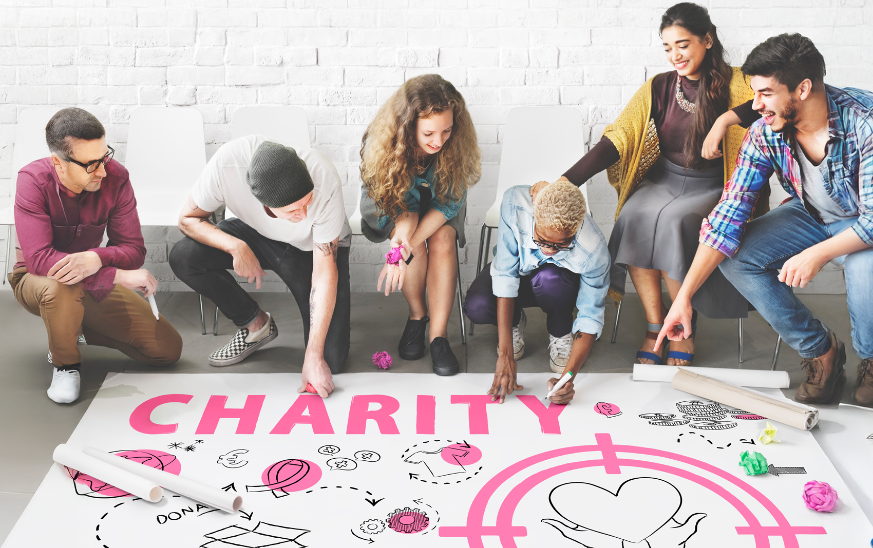 Group of diverse people brainstorming on a large poster on floor that says Charity.