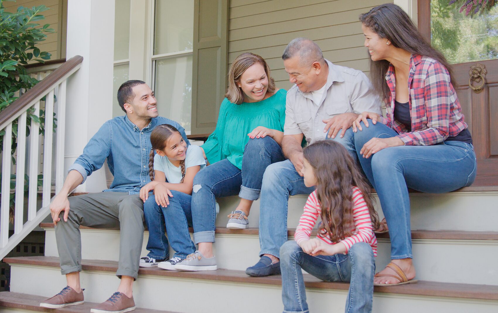 Happy multi-generational family sitting on porch steps outside.