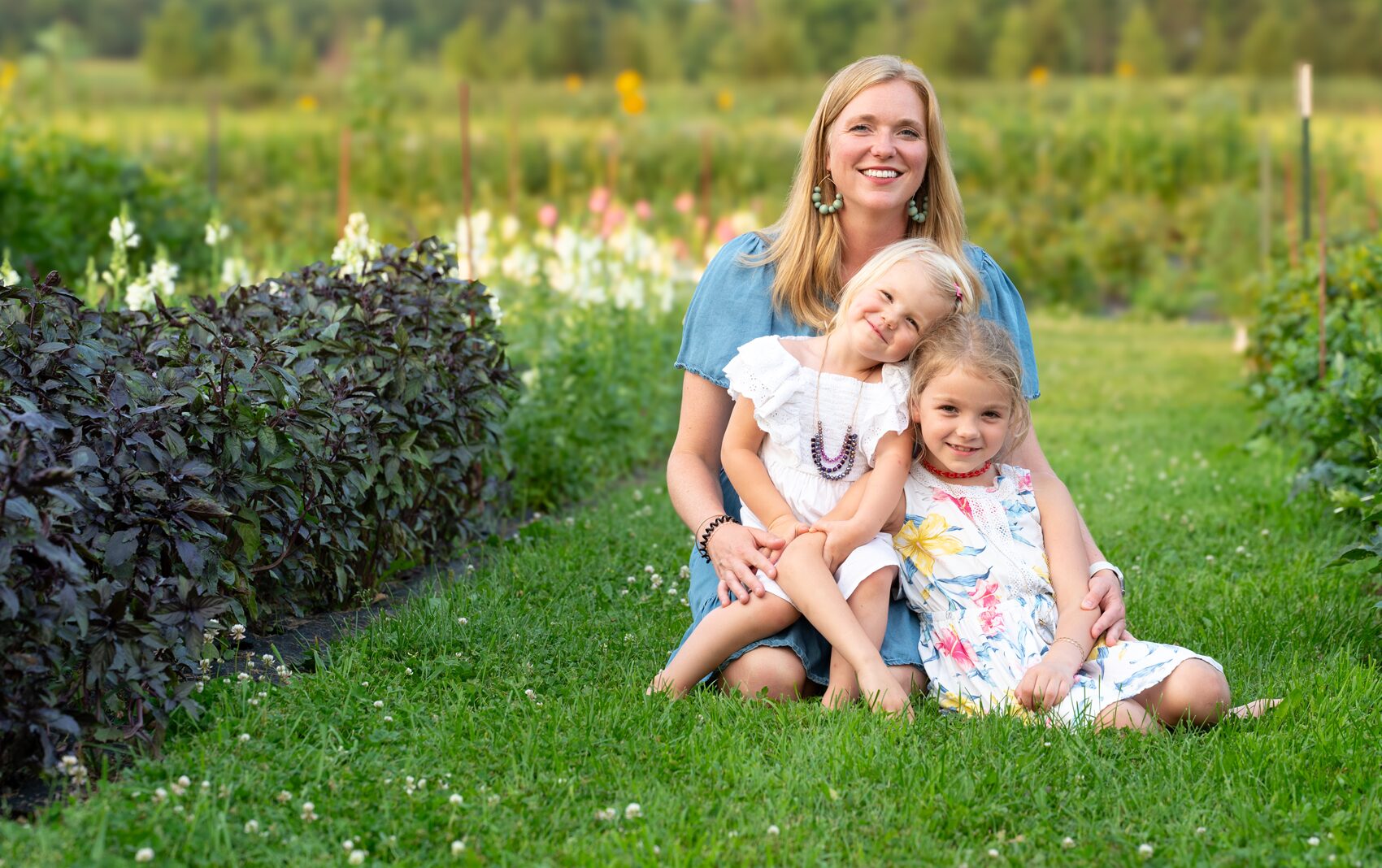 Happy blonde woman with two small daughters sitting on grass.