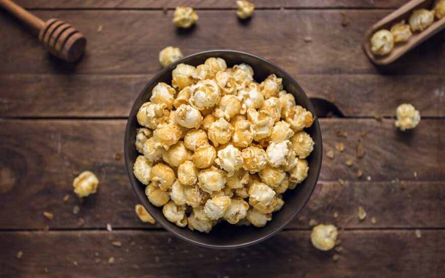 Close up of honey crunch popcorn in a brown bowl on a wooden table.