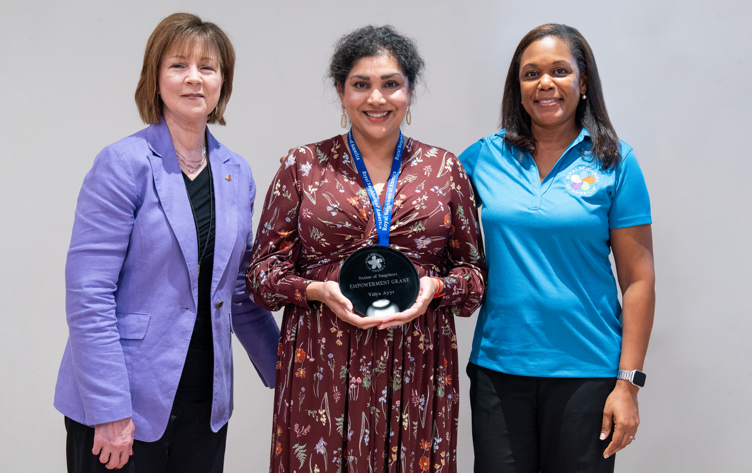 Three happy women, center woman is holding a black circular Nation of Neighbors award.