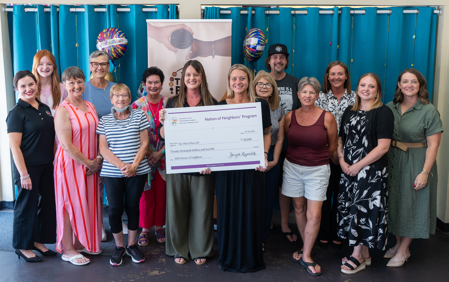 Large group of happy people with a giant check and a teal curtain in the background.